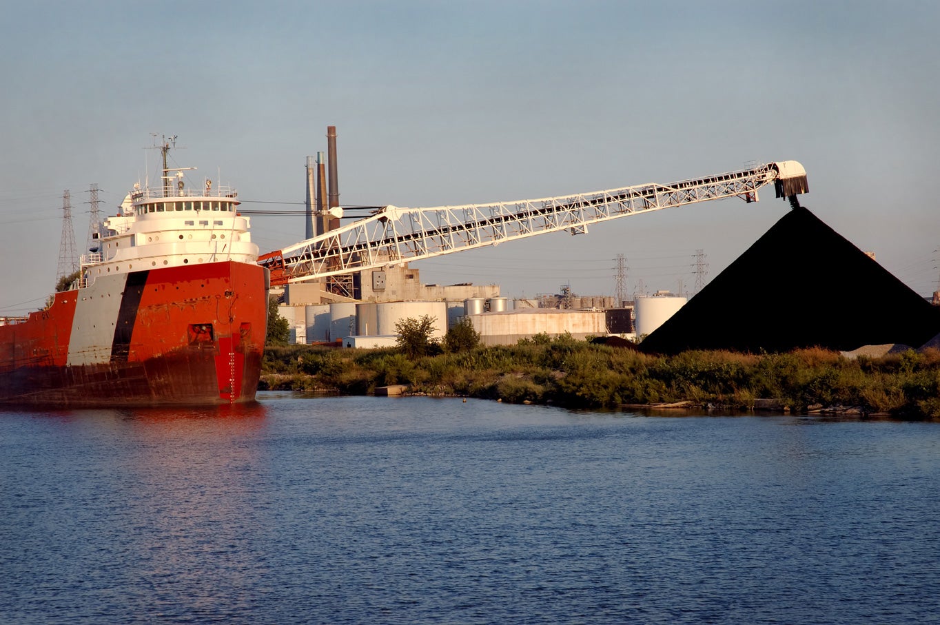 A coal ship unloads near the water.