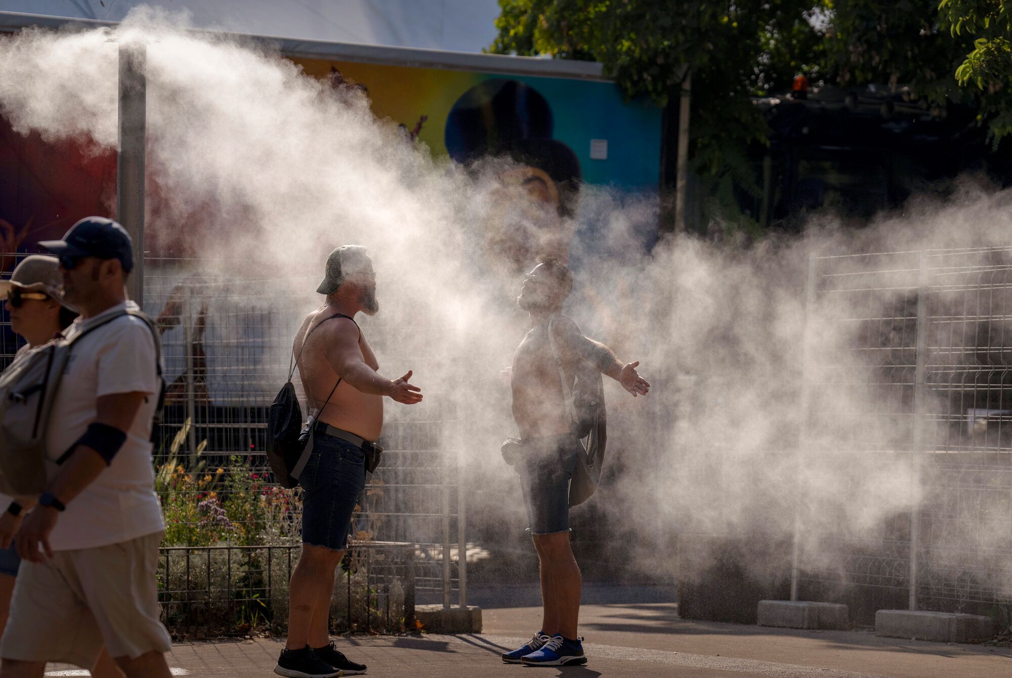 Двое мужчин охлаждаются водой из общественного пульверизатора в жаркий и солнечный день в Барселоне 16 июля 2022 года, когда рекордные температуры и лесные пожары охватили Западную Европу.