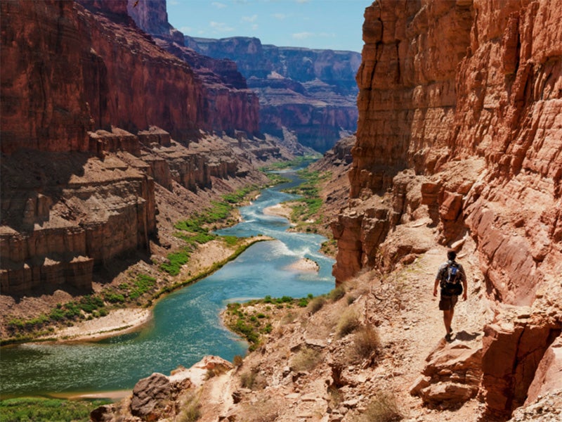 A hiker walks along the Colorado River.