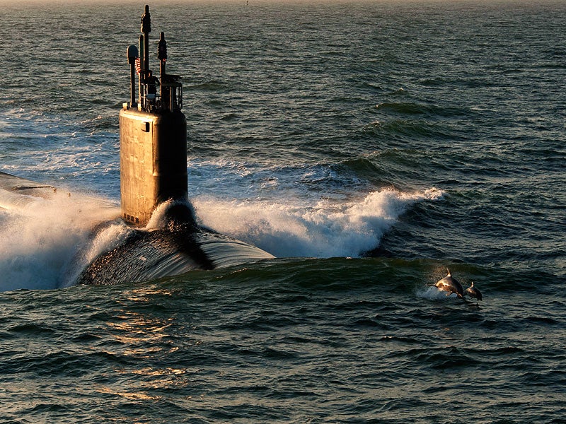 Dolphins swim in advance of Virginia-class attack submarine PCU Minnesota.