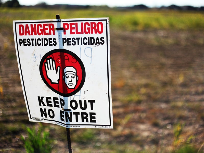 A sign warns of pesticide application in a farm field.