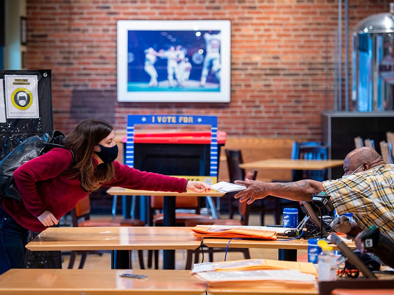 A volunteer (right) helps a woman register at an early voting station at Camden Yards, on the second day of early voting in Baltimore, Maryland, on October 27, 2020. A volunteer (right) helps a woman register at an early voting station at Camden Yards, on the second day of early voting in Baltimore, Maryland, on October 27, 2020.