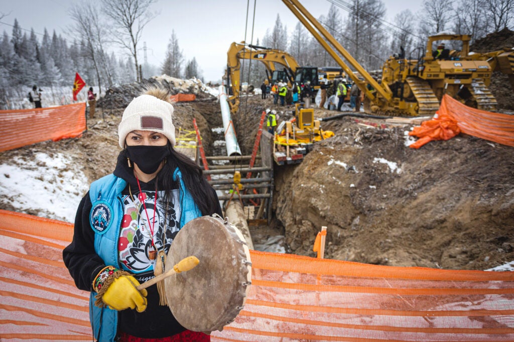 Gio Cerise, a member of the White Earth Nation, plays a drum and prays in front of Line 3 pipeline construction on Highway 169 south of Hill City, Minn.
