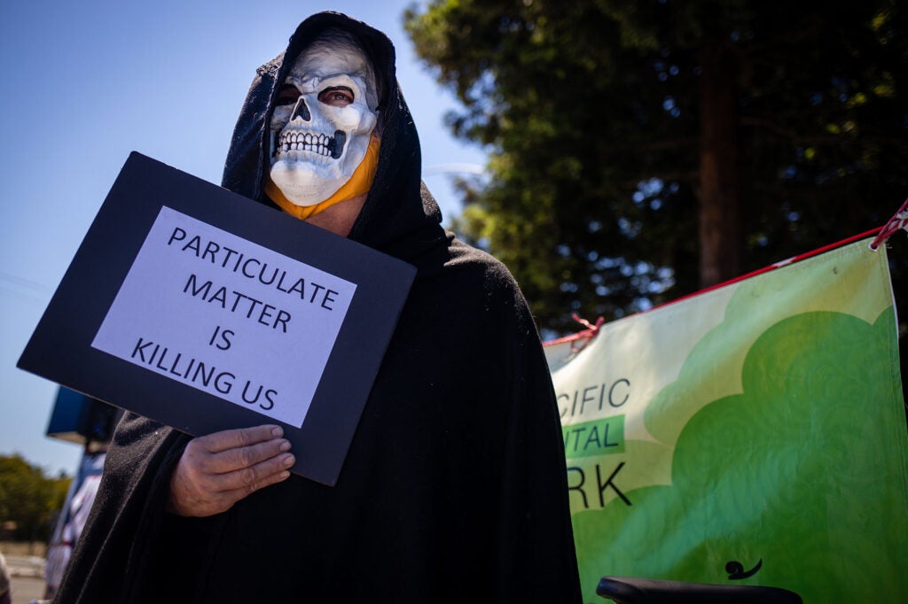 A man who identified himself as Death holds a sign at a protest in in front of the Chevron Oil Refinery in Richmond, Calif., on May 21, 2021.