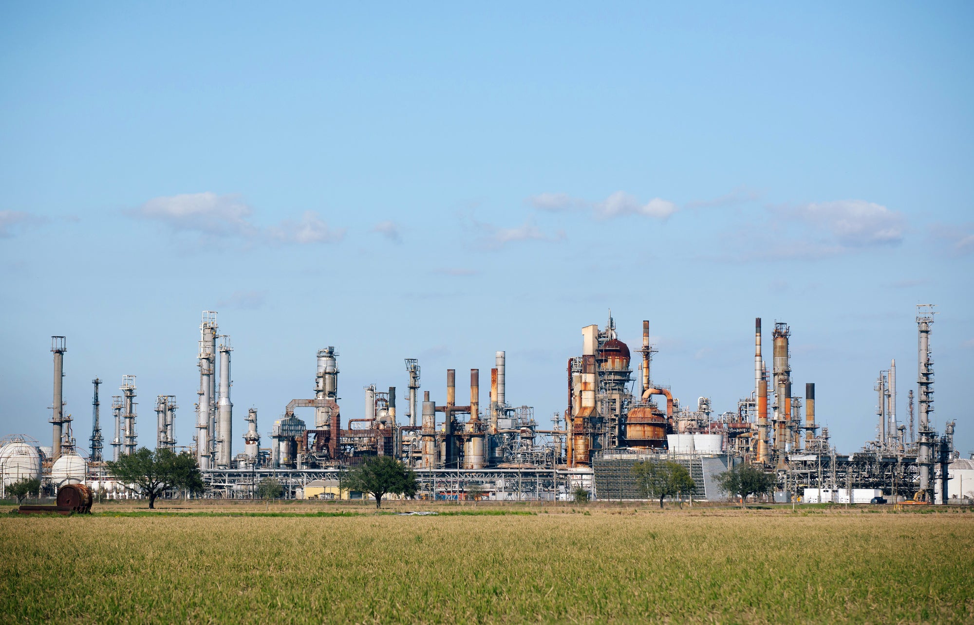 Fossil fuel refinery with a blue sky and field in foreground.