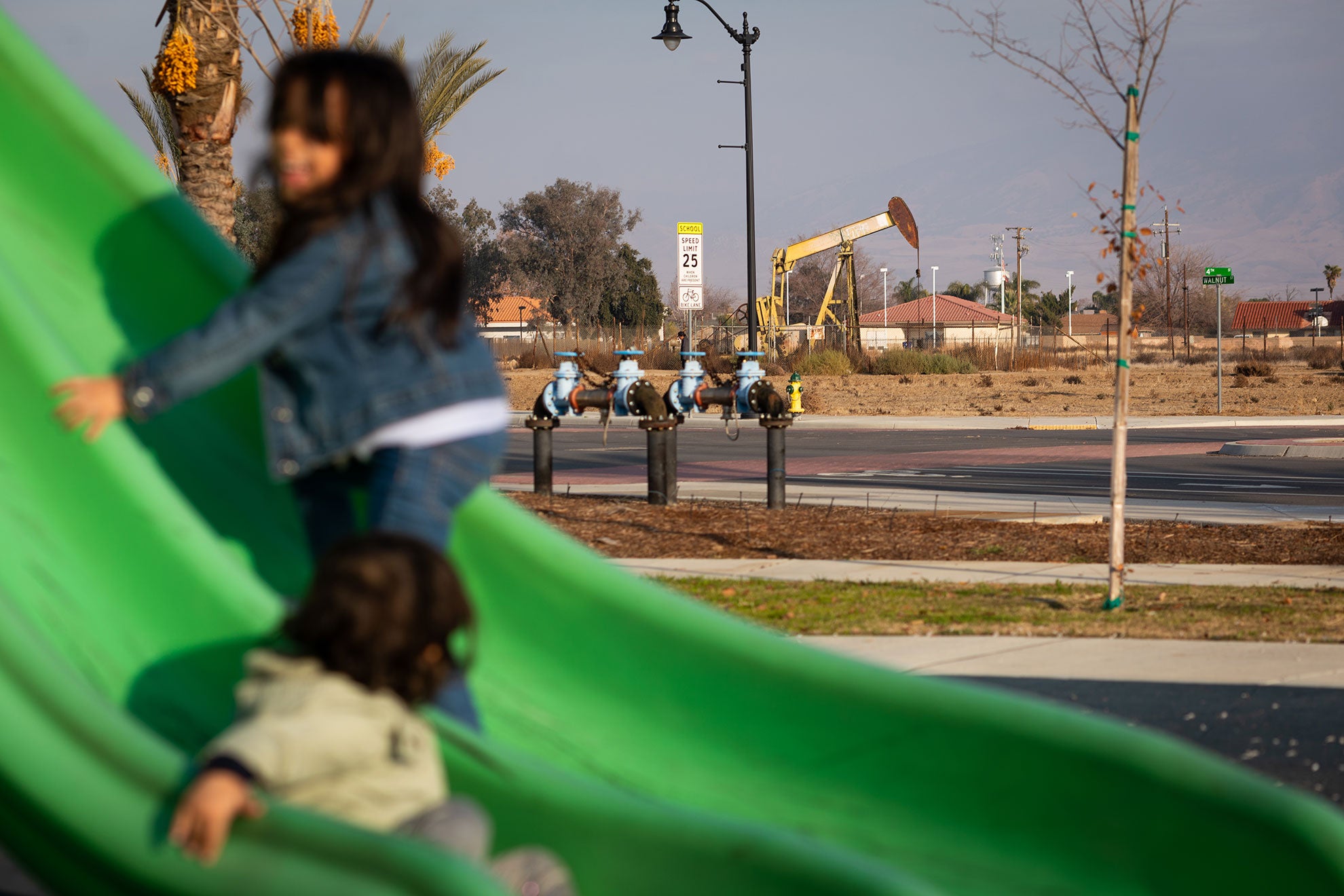 Children play at Arvin's “Garden in the Sun” playground. There are several oil wells near the park.