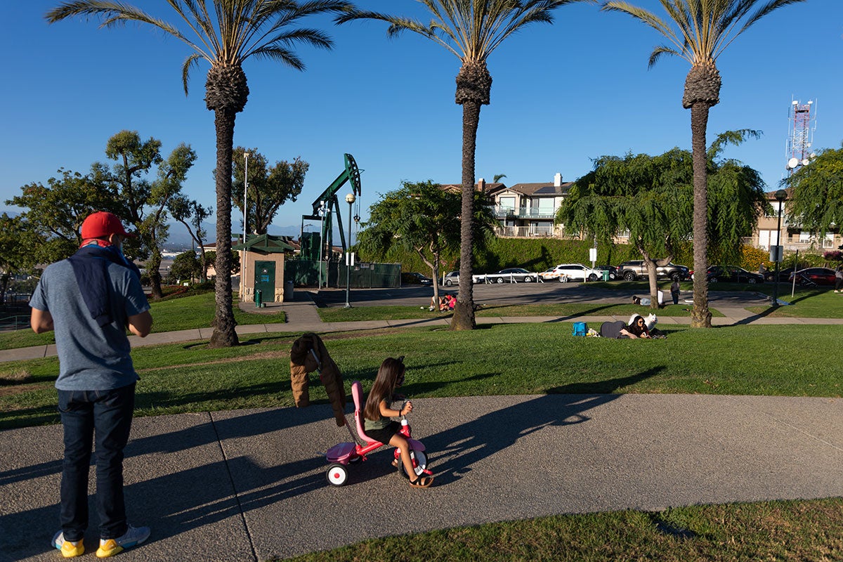 At Signal Hill's Hilltop Park, an active oil derrick operates among visitors, tourists, and nearby houses.