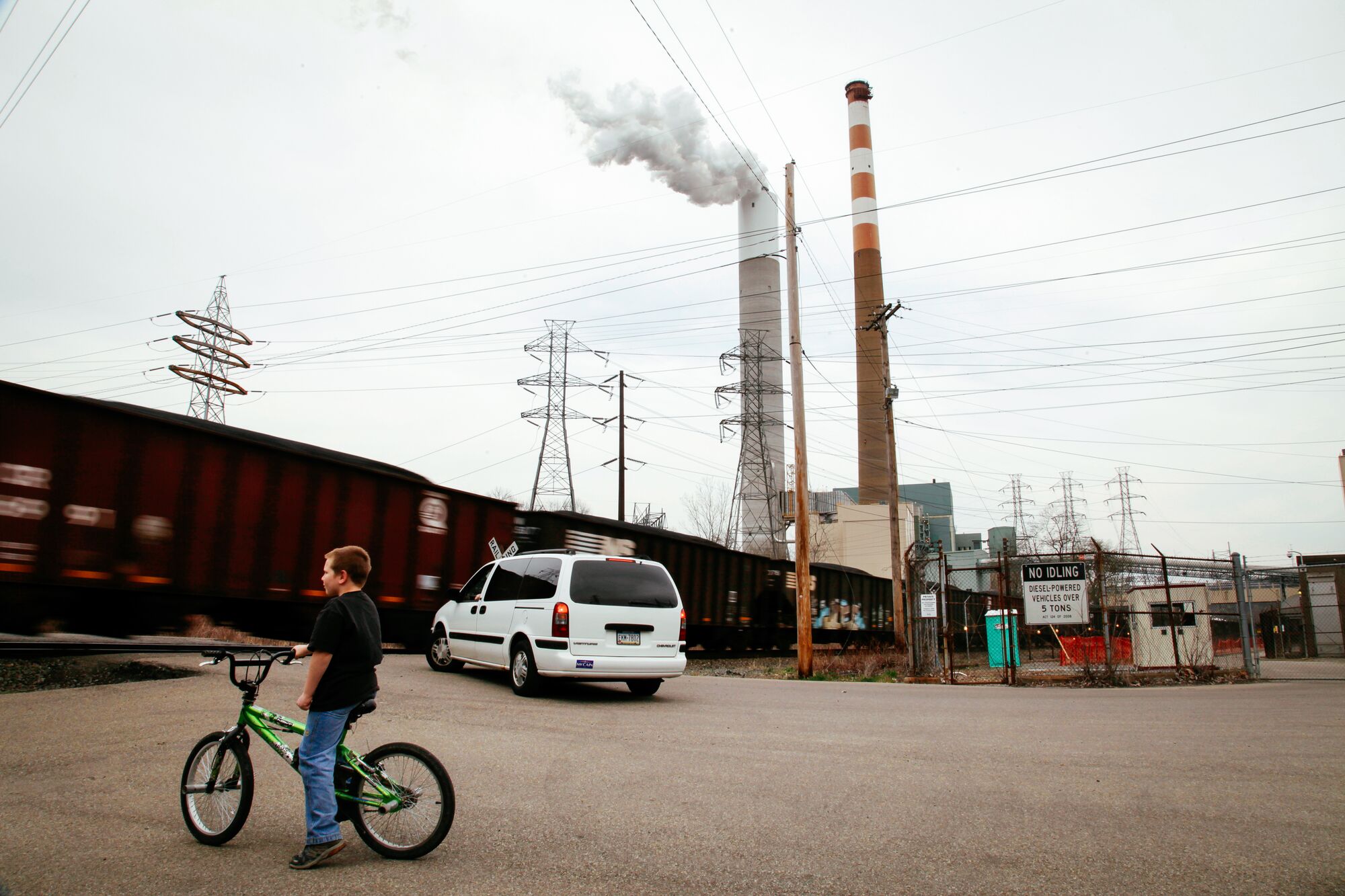 A young child and van wait at a railroad crossing for a train to pass, under the shadow of the Cheswick Generating Station in Springdale, Penn.