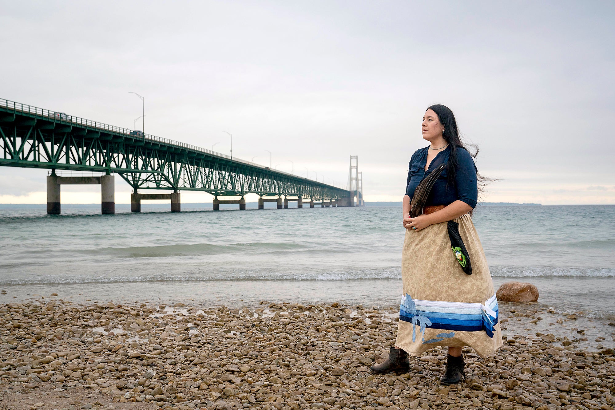 Whitney Gravelle standing on the lake's shore, with a bridge and water in the background.