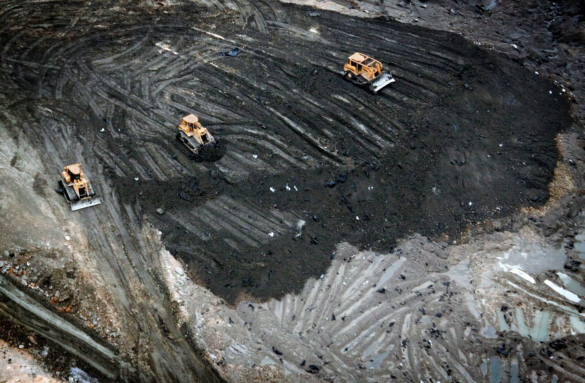 Bulldozers pushing black coal ash, photographed from above