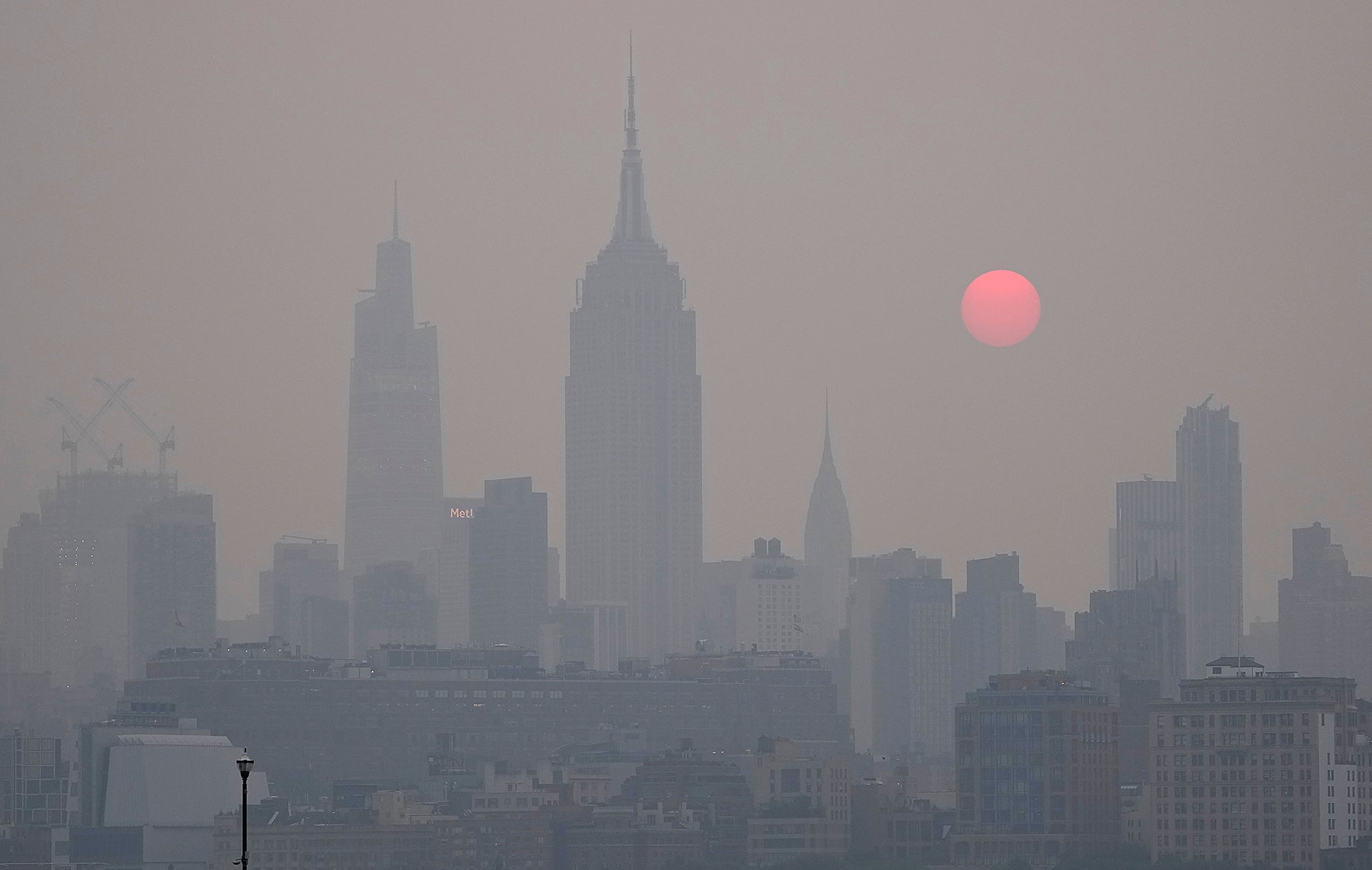 Gray smoky New York skyline with a large orange sun rising behind it.