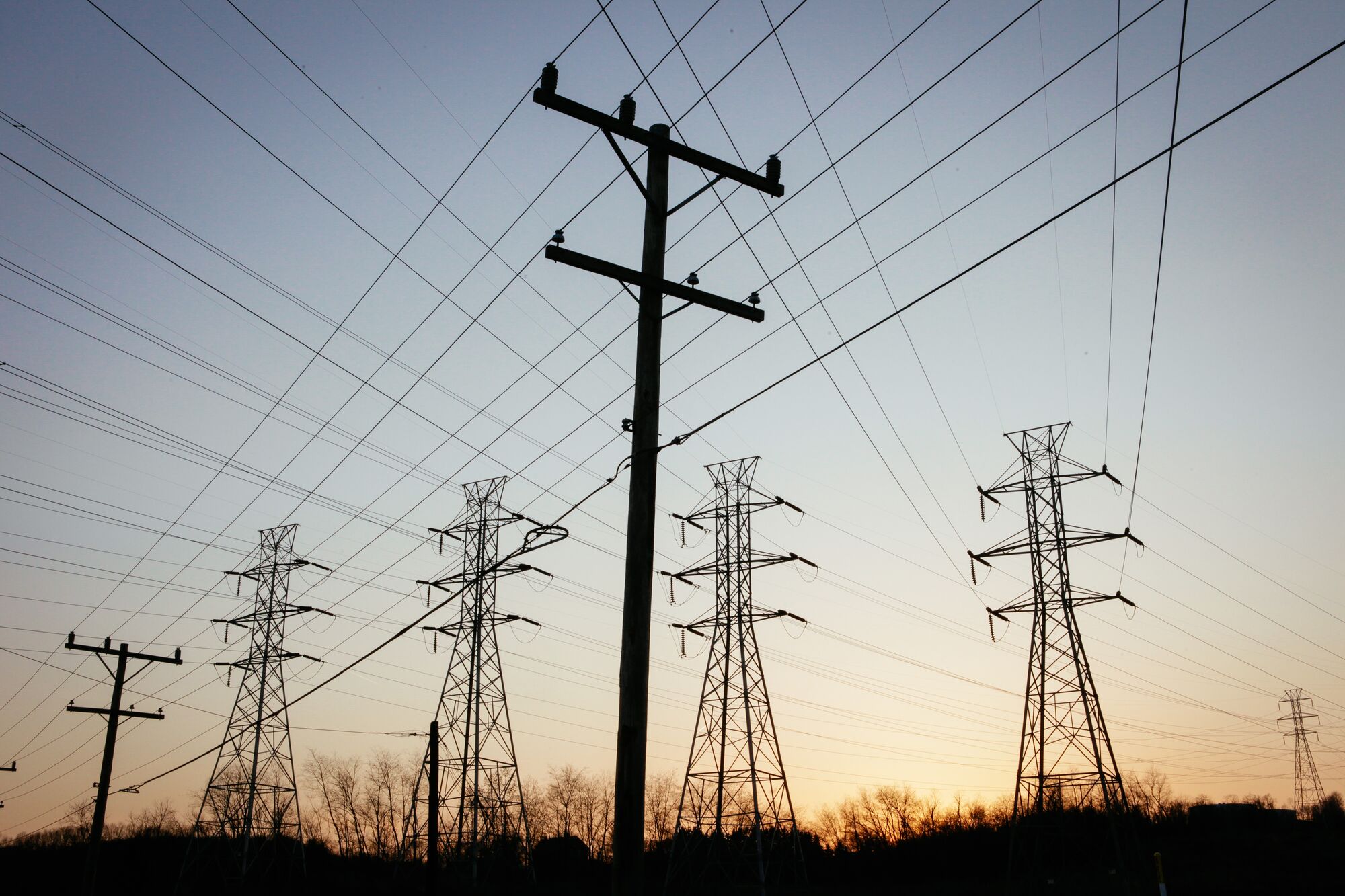 Transmission lines and utility poles are silhouetted at sunset against a darkening sky.