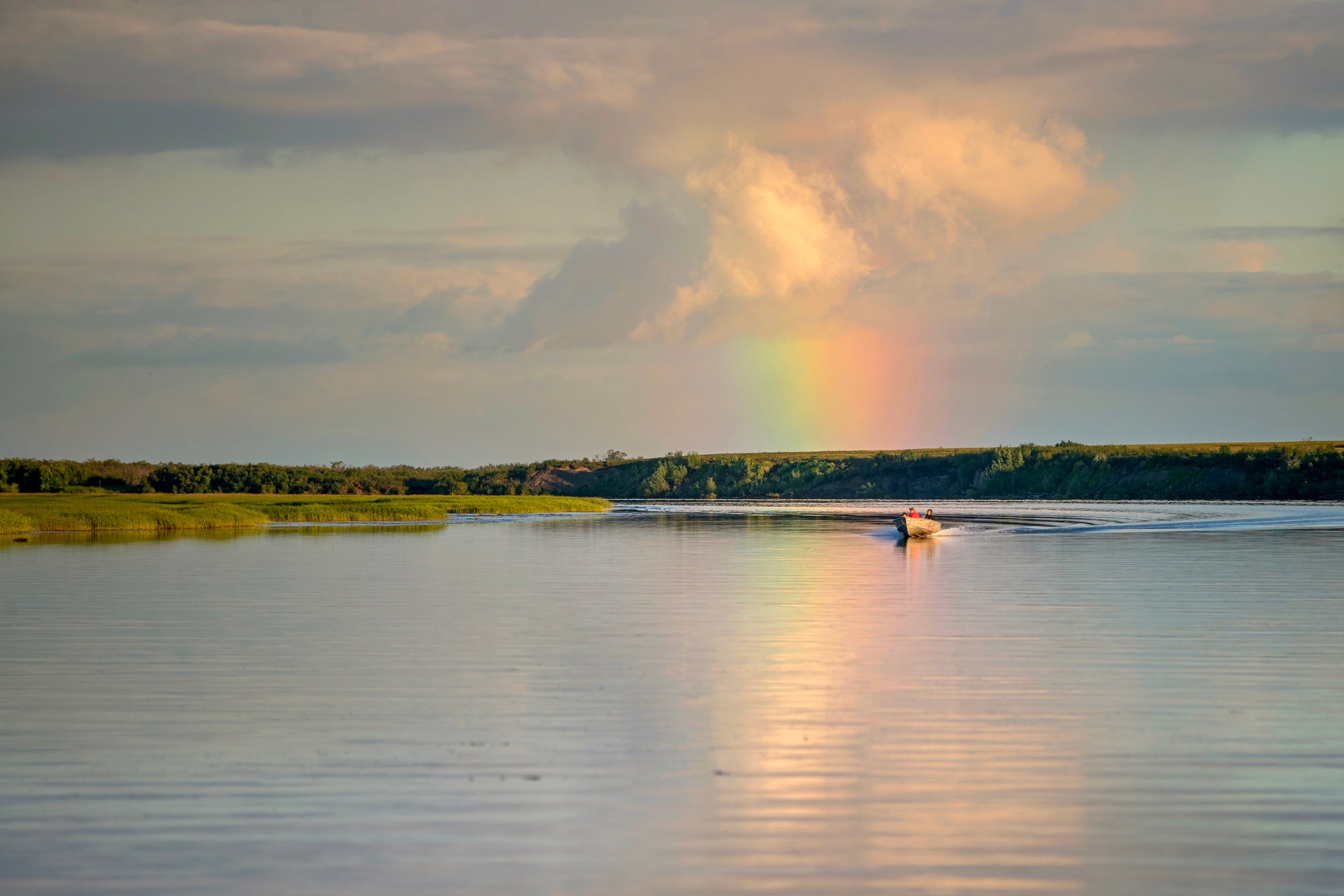 Donlin Mine a small boat with several people on a wide, smooth river with a rainbow in the background.