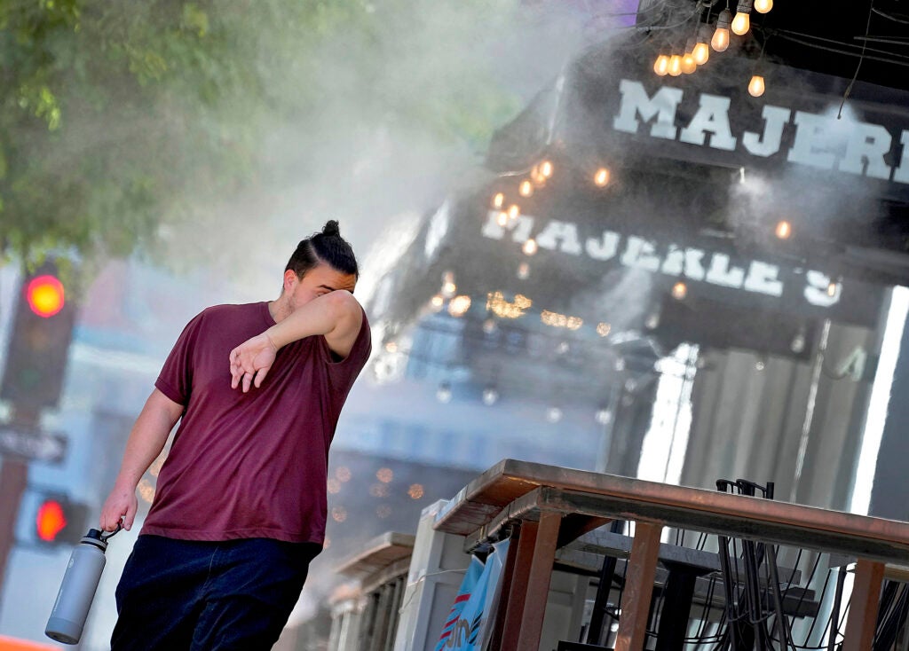 A man wipes his brow as he walks under misters on July 13, 2023 in downtown Phoenix. Arizona, Nevada, New Mexico and Southern California are getting hit with 100-degree-plus temps and excessive heat warnings. (Matt York / AP)
