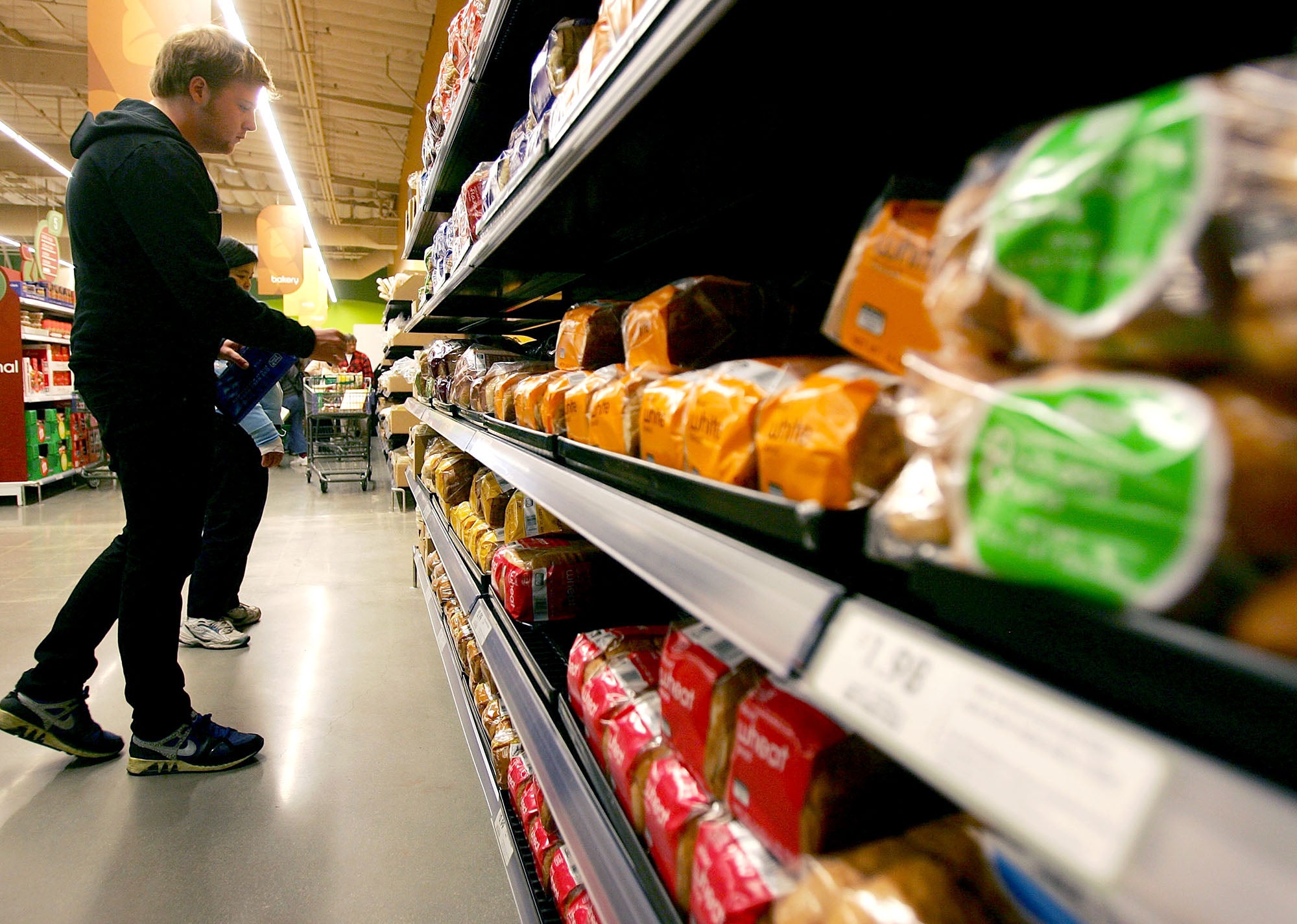 A man looking at several shelves of bread at a grocery store
