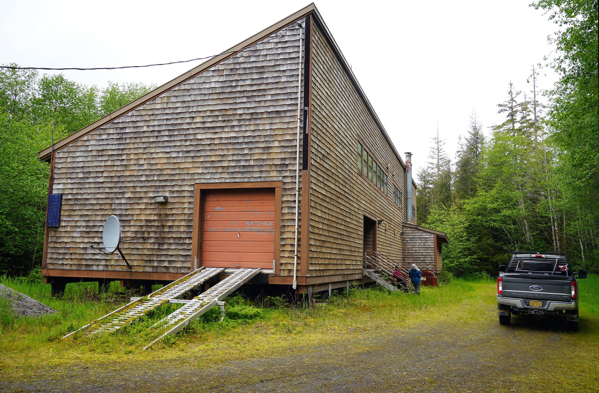 A large wood shingled building with an angled roof in the woods.