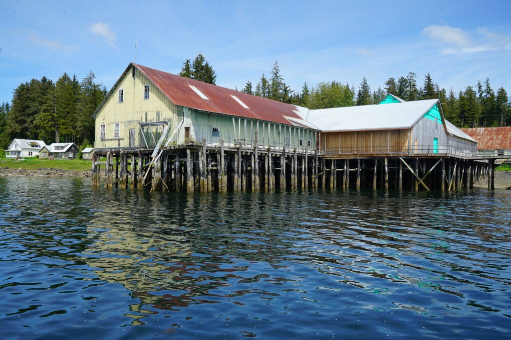 A building built on a pier over the water, looking back on land with homes in the background.