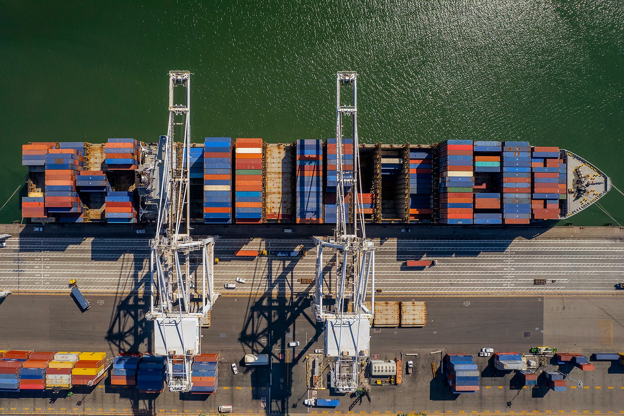 Overhead view of a large container ship with cranes above it.