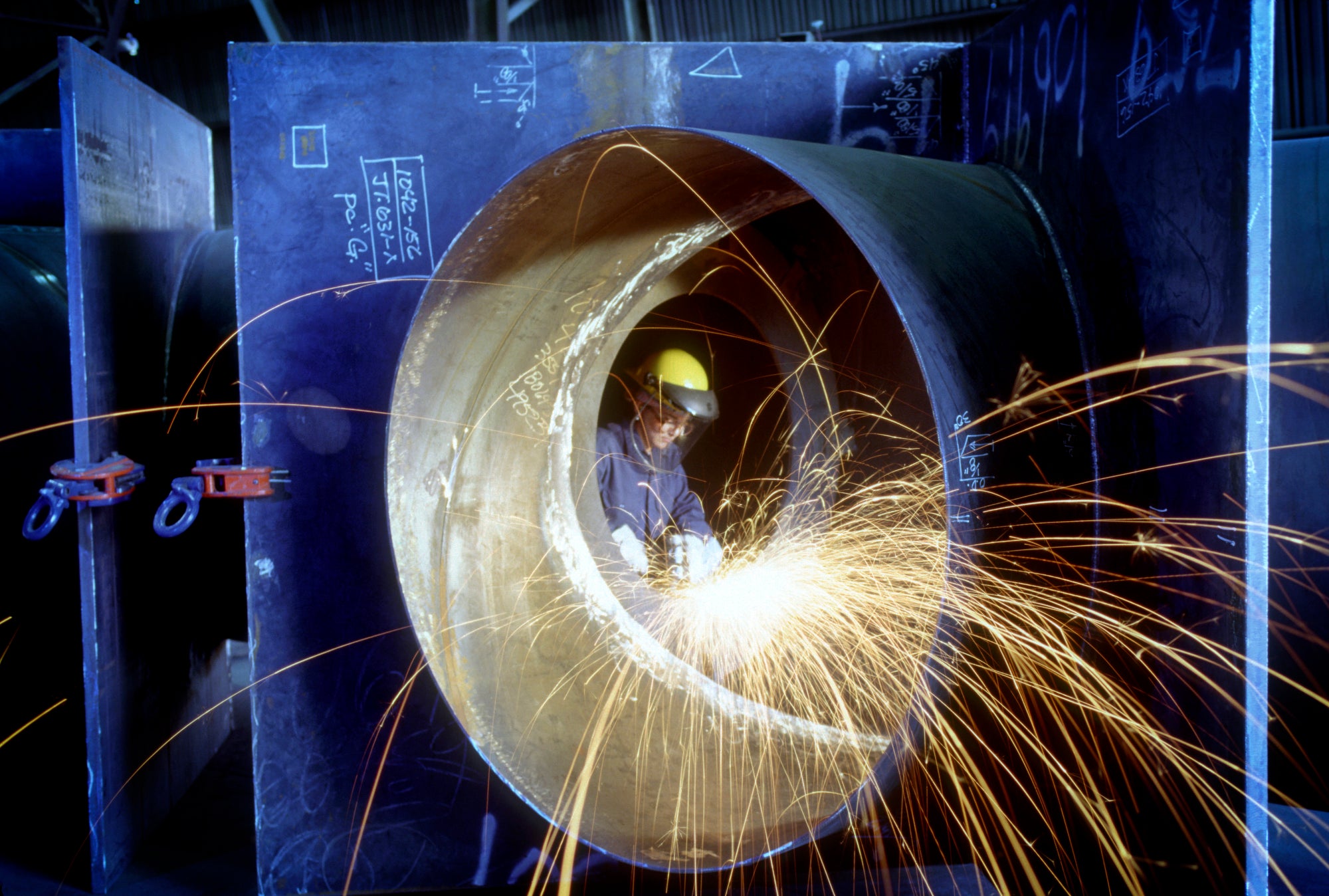 sparks fly as a person welds inside of a large pipe