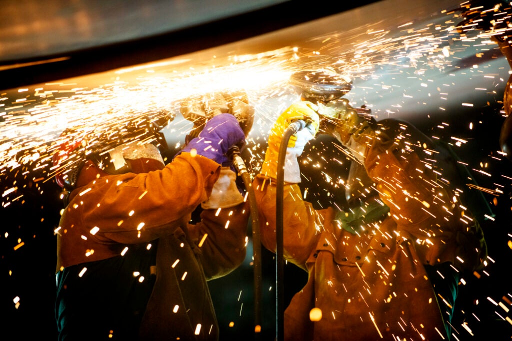 Two workers working overhead with sparks flying around them.