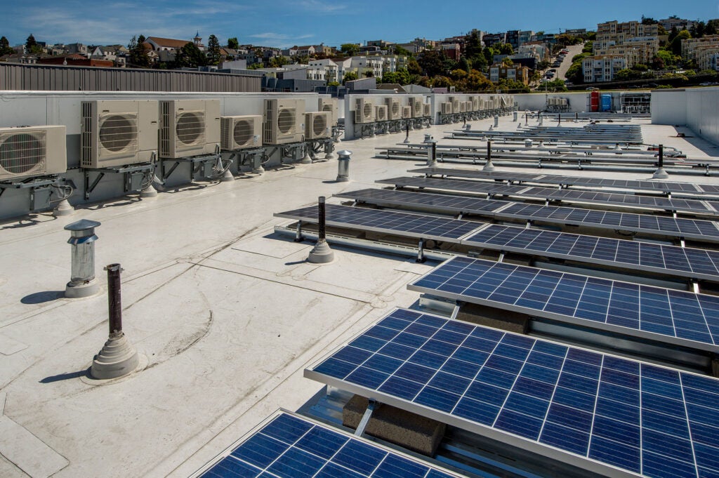 Rooftop heat pumps on an apartment building, with rooftop solar panels in the foreground.