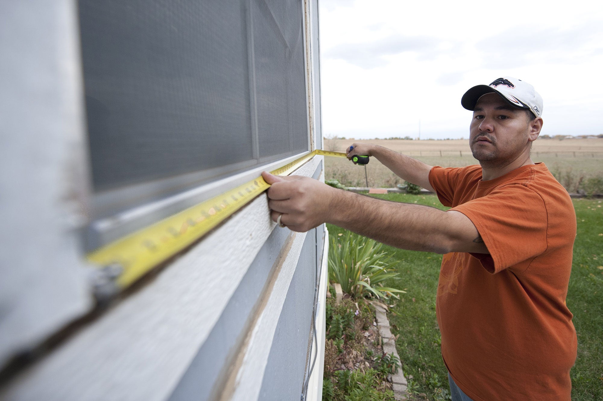 A homeowner stretches out measuring tape along the bottom of a window frame outside of their home.