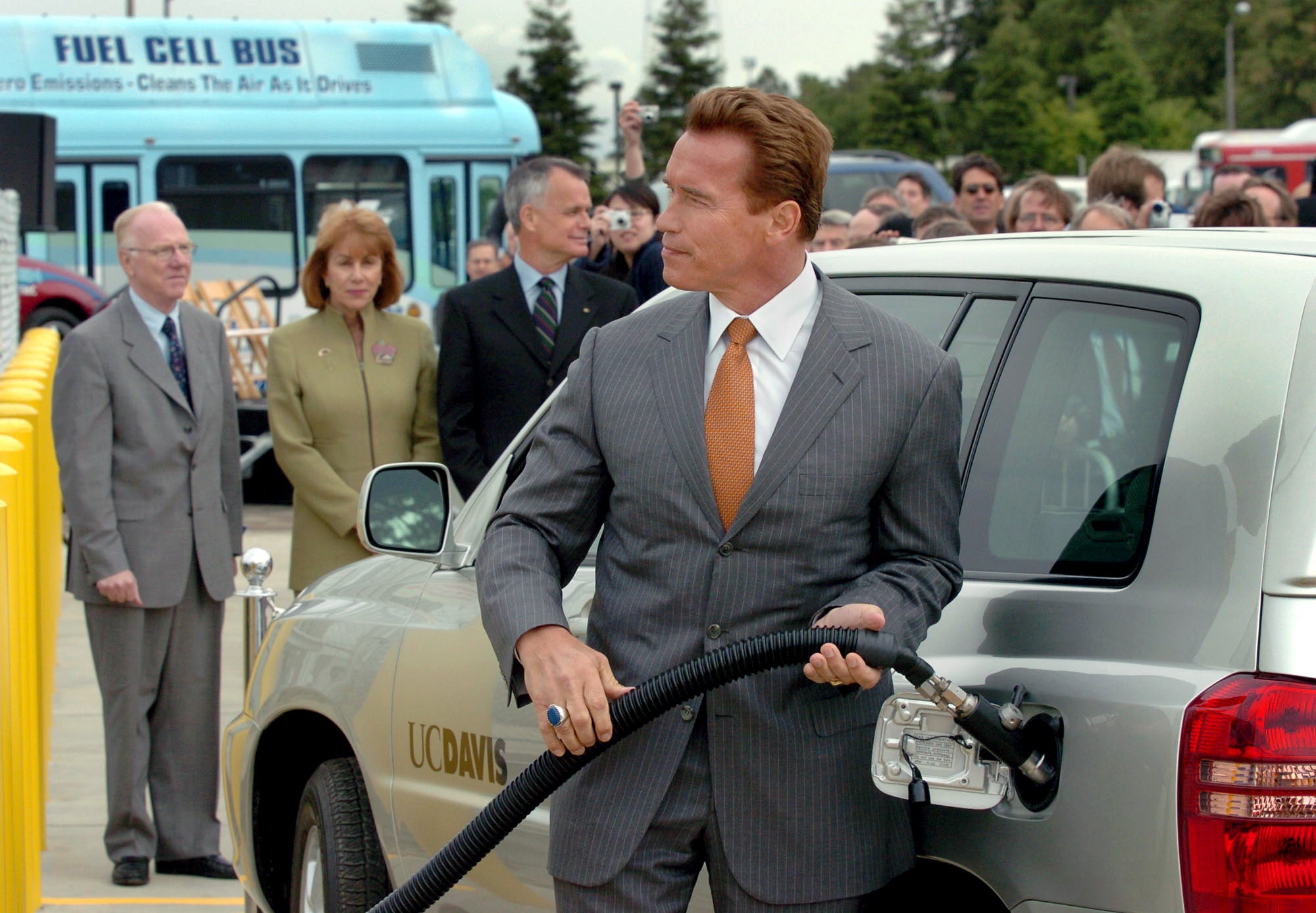 Schwarzenegger, wearing a suit, fills up a car.