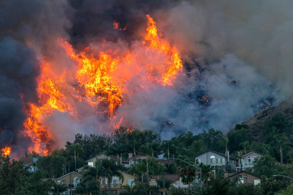 Large flames on a hillside looms just above homes below it.