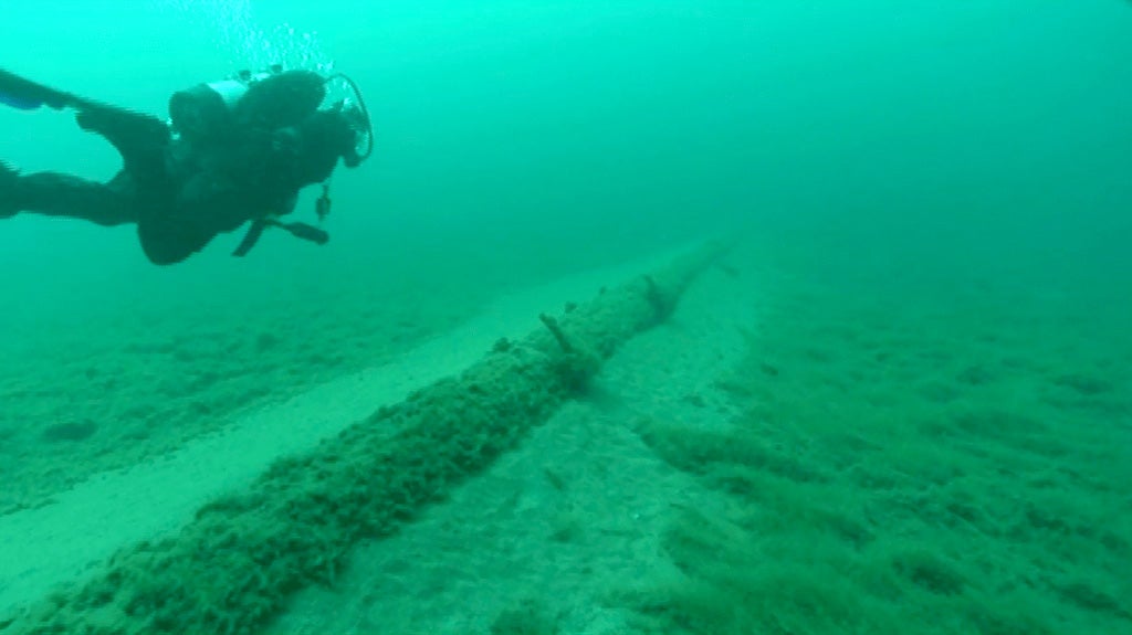 A diver swimming near a large pipe on the floor of a lake