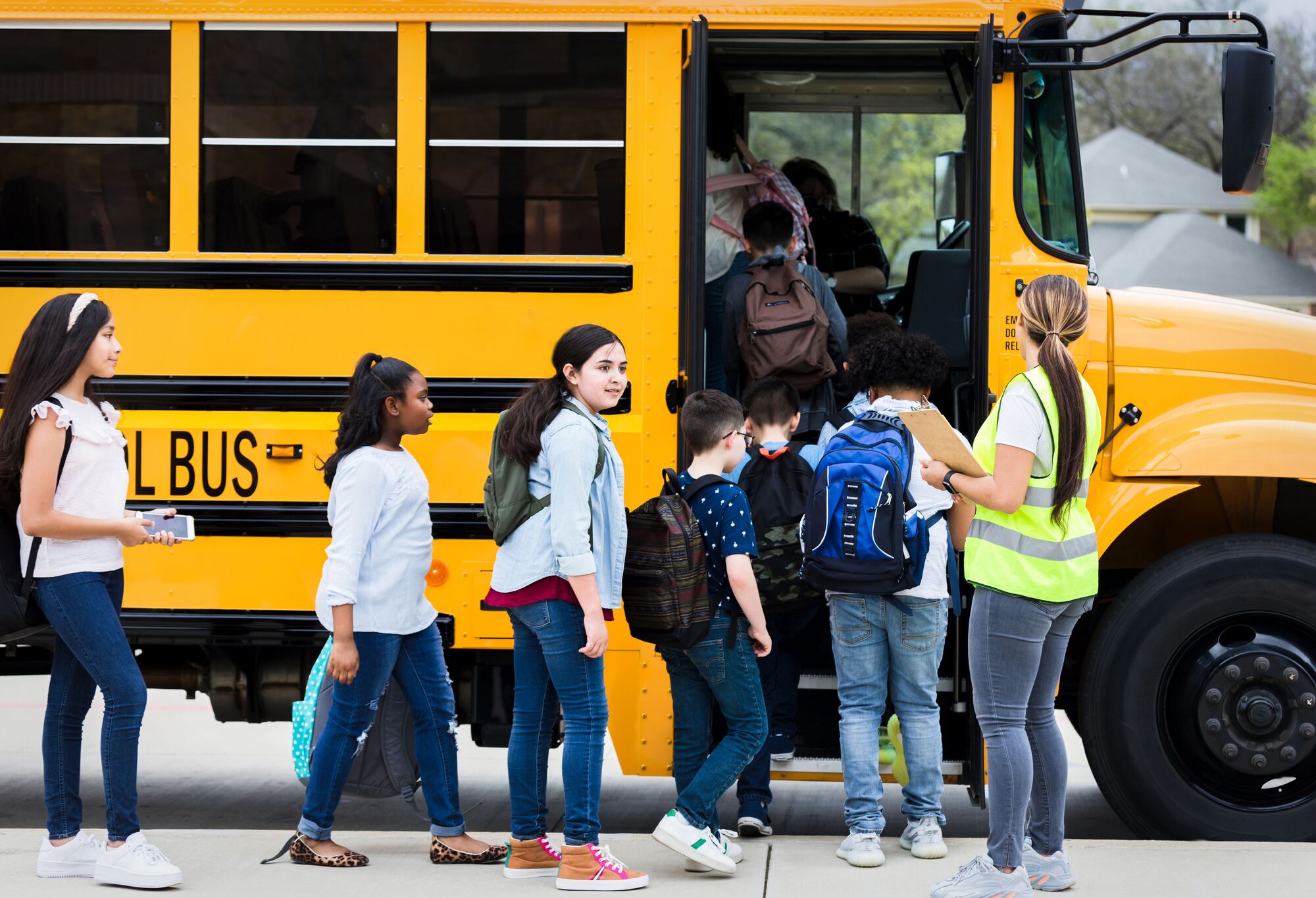 Led by a chaperone, a group of school children board a yellow school bus.