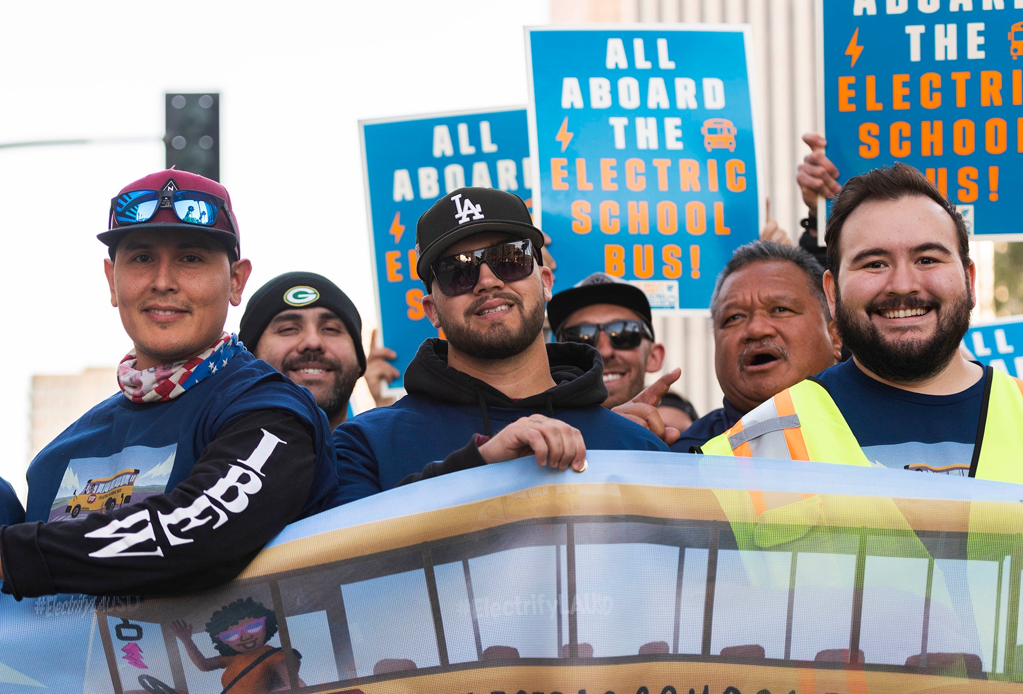 Men hold signs and smile during an outdoor rally