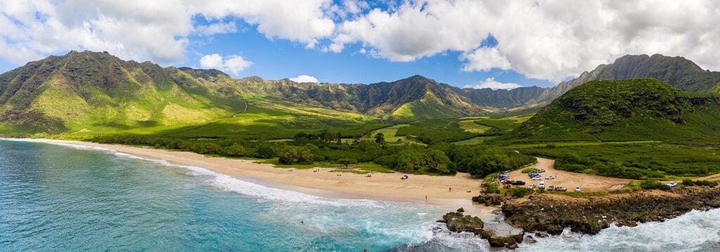 A wide photo of a beach, surrounded by a green valley in Hawaii.