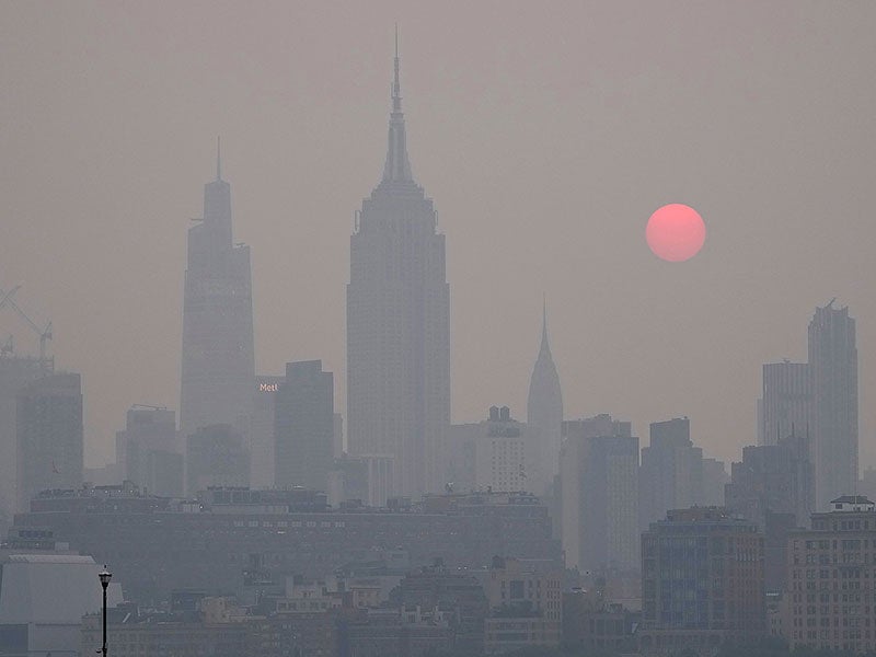 Gray smoky New York skyline with a large orange sun rising behind it.