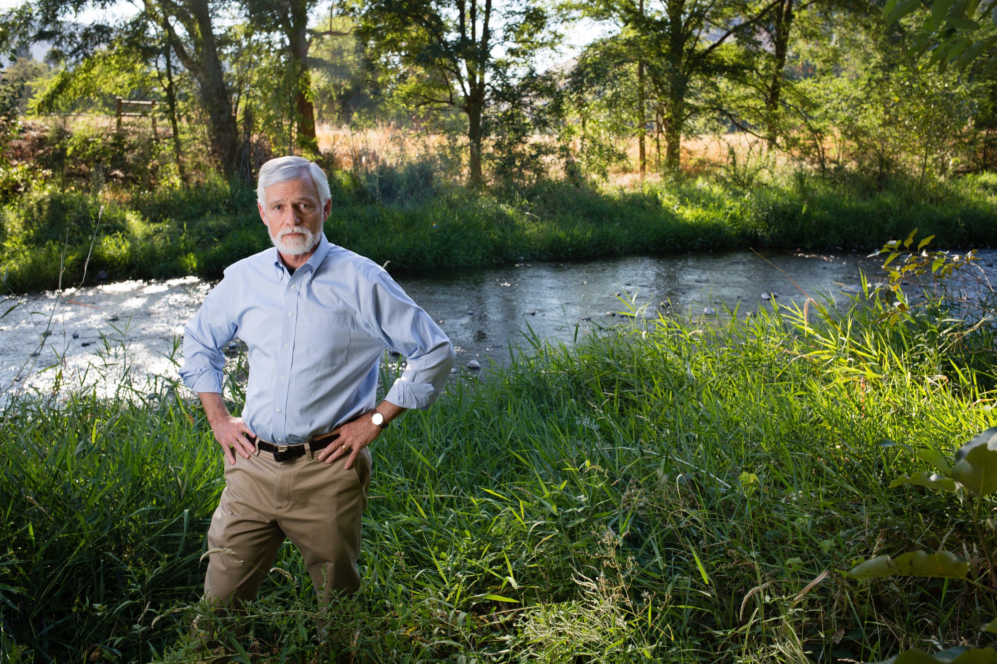 Portrait of a man looking directly at the camera, standing next to a river.
