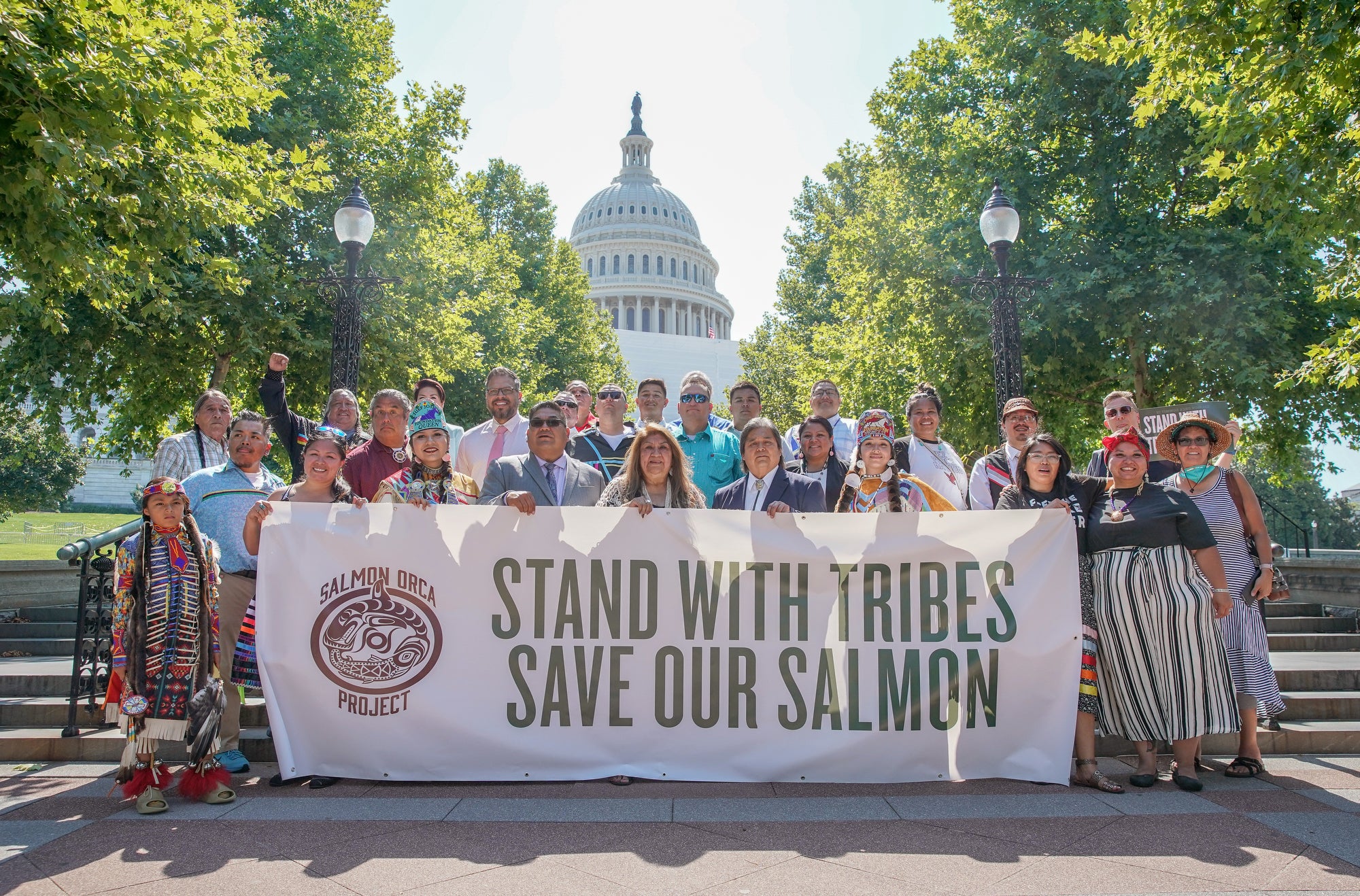 A group of people stand in front of the U.S. Capitol with a banner that reads "Stand with tribes save our salmon"