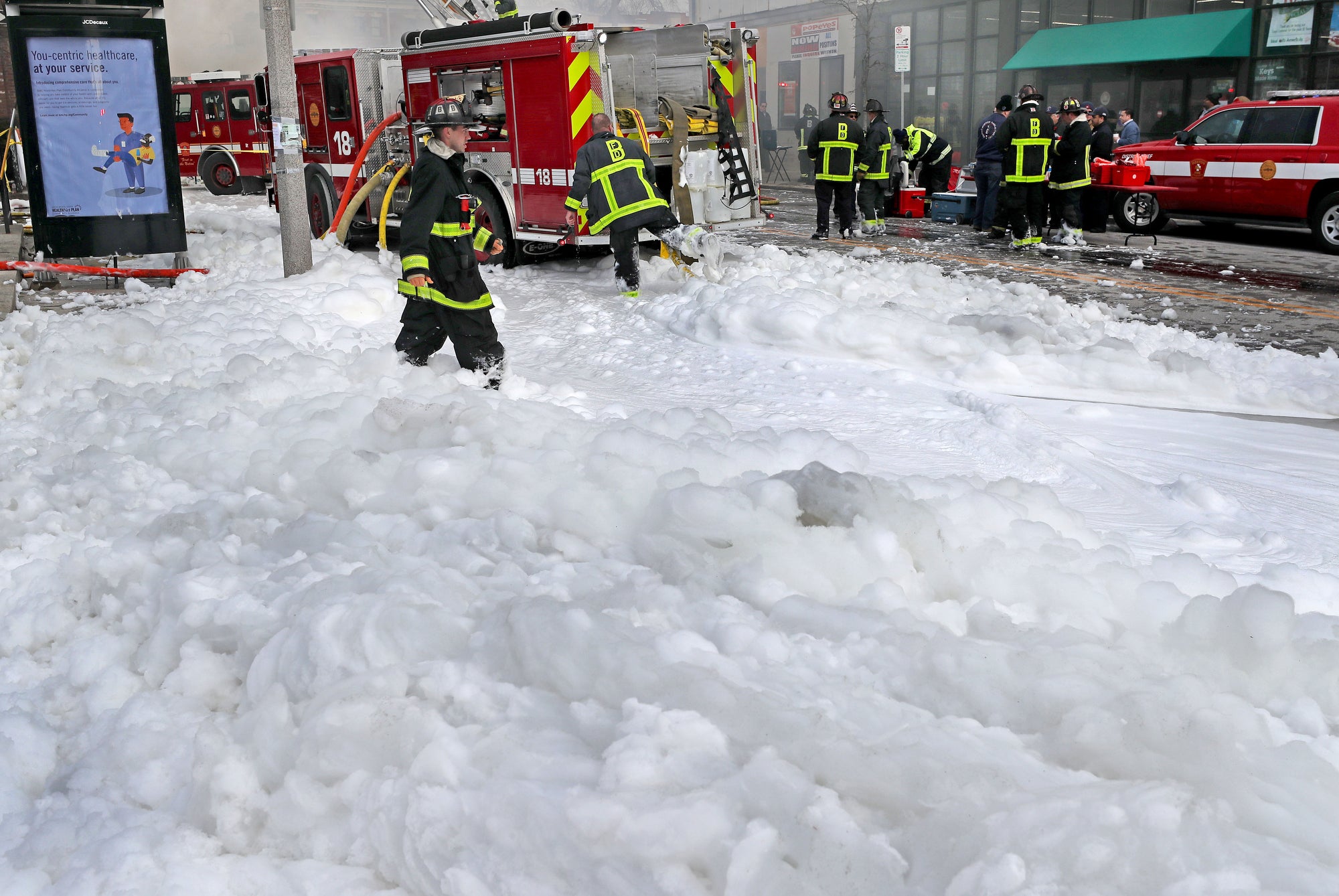 Firefighters wade through a thick layer of foam while cleaning up after a fire on a city street
