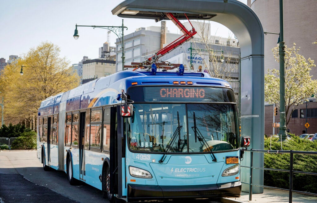 A bus connected to an overhead charger on a city street.