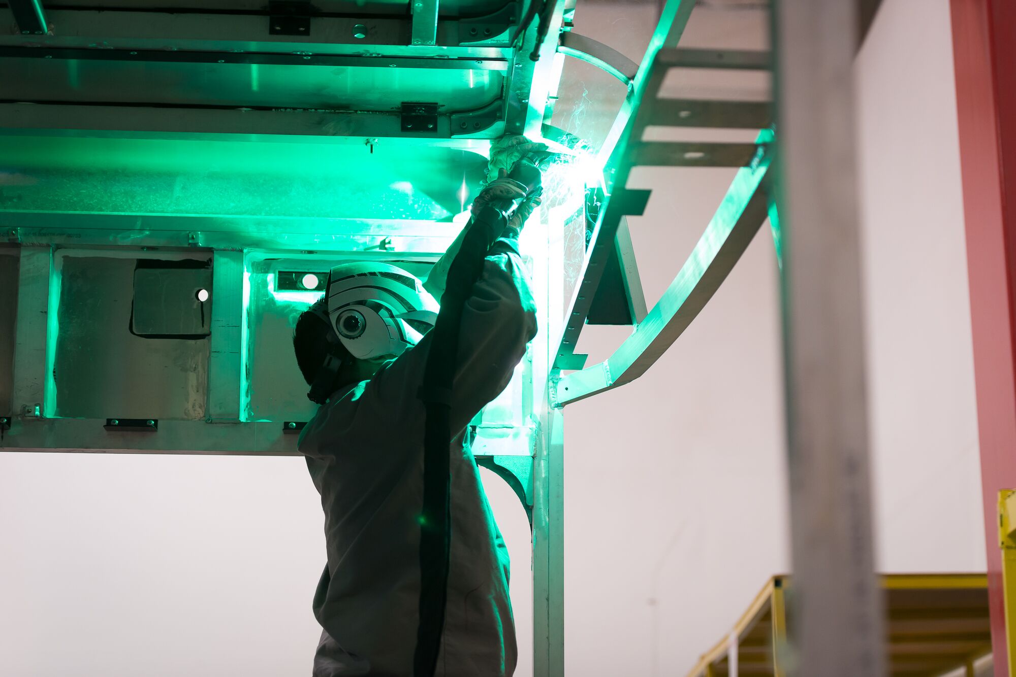 A technician wearing a protective welding mask works on building the frame of an electric bus.