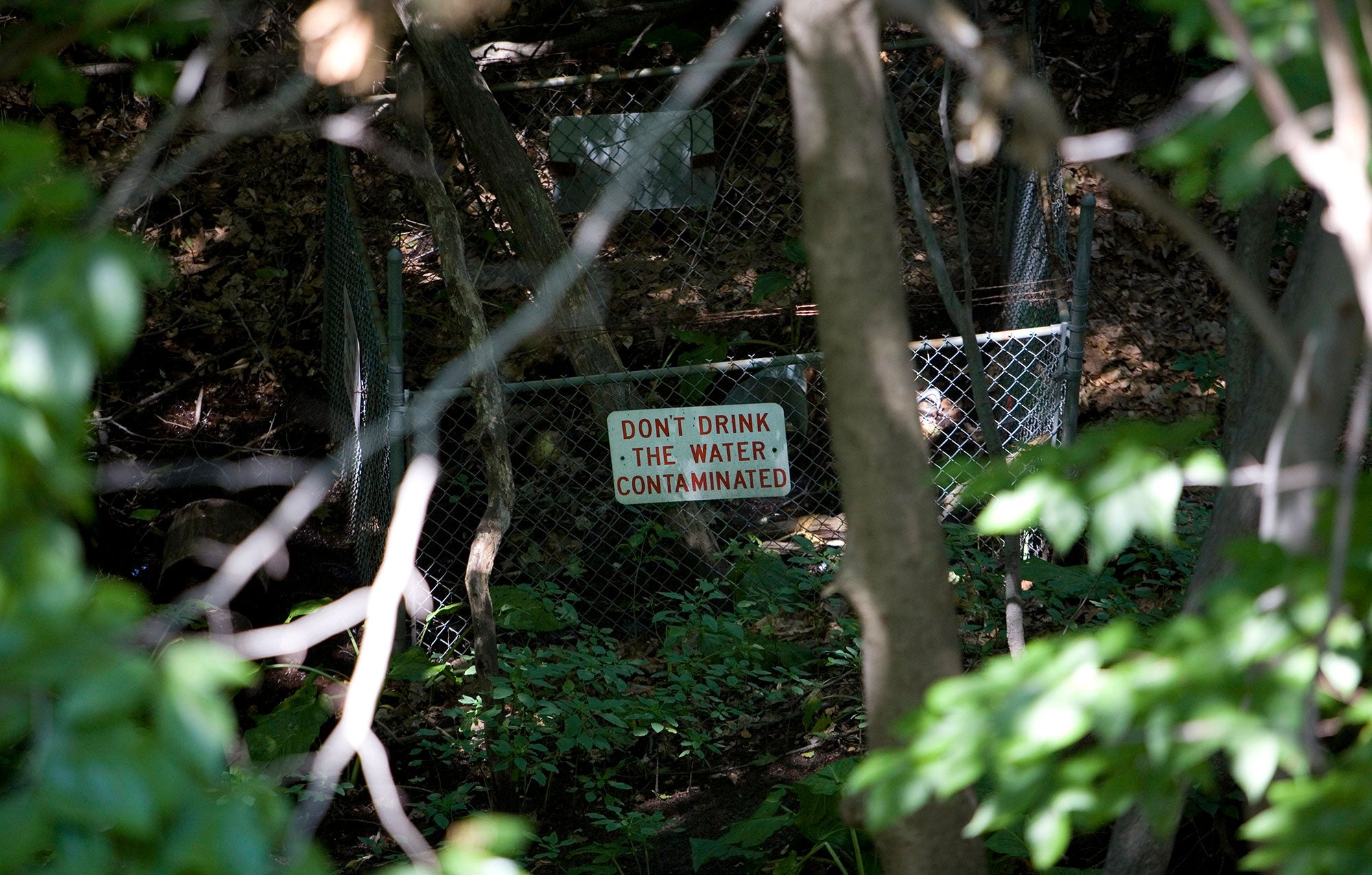 A sign ("Don't drink the water. Contaminated") on a chain link fence warns visitors from a stream contaminated with trichloroethylene (TCE) in Fort Edward, N.Y.