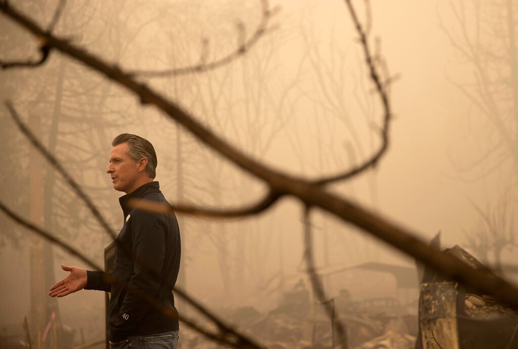 Gavin Newsom speaks in a burned and smokey area.