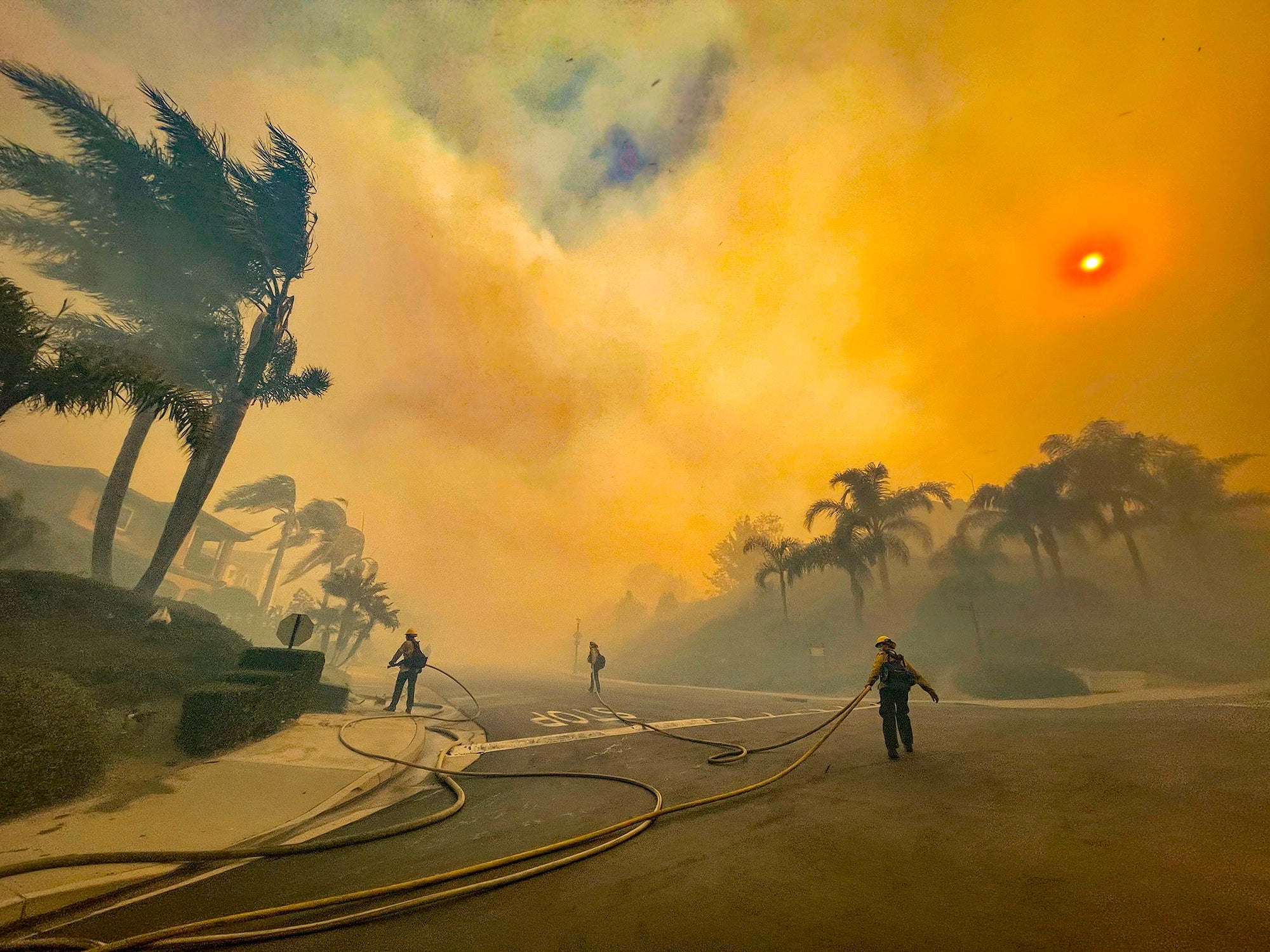 Firefighters walk in a neighborhood filled with orange smoke.