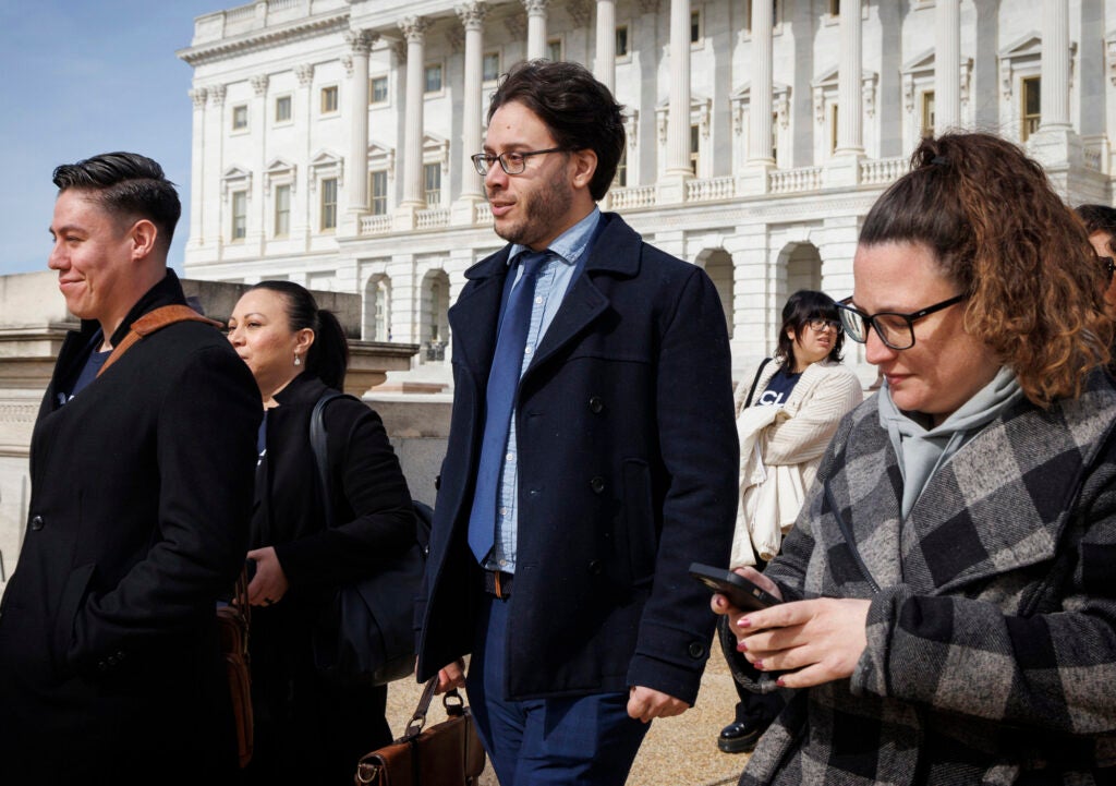 A group of people walk outside, near the U.S. capitol building.