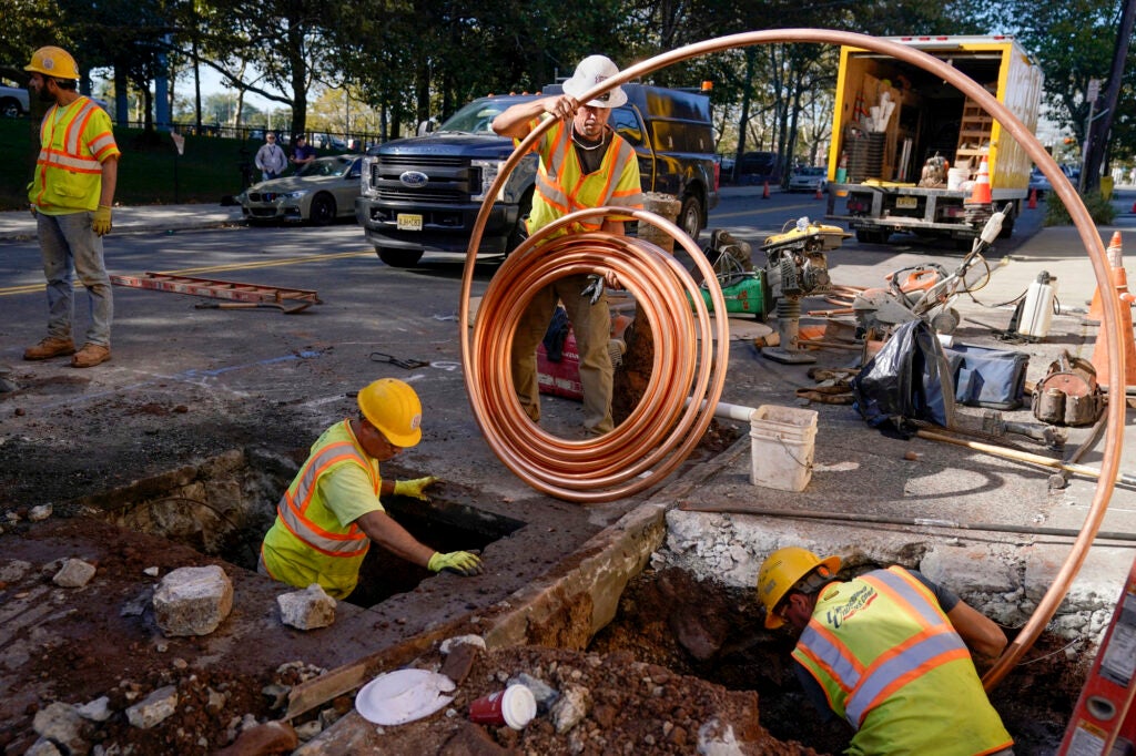 Workers install new copper piping from a larger spool.