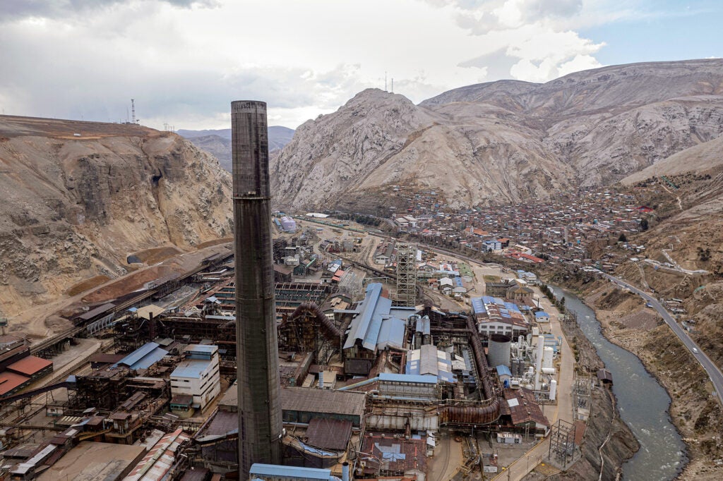 A large industrial facility and smoke stack in the foreground with a collection of smaller homes and buildings near it.