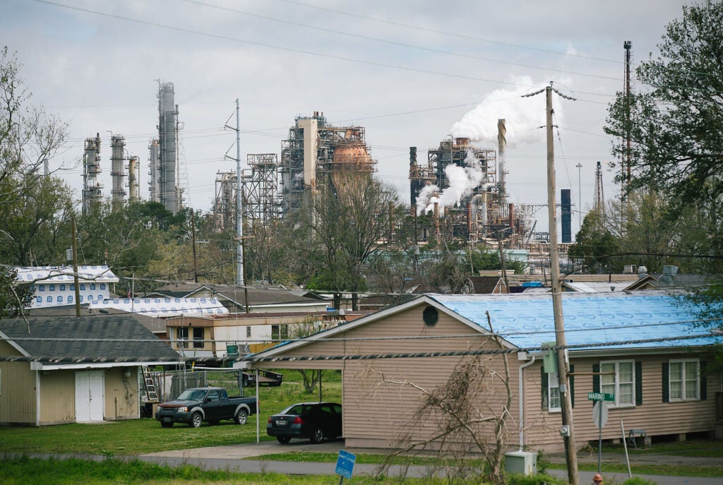 Small homes are pictured near a large refinery complex releasing smoke and vapors behind them.
