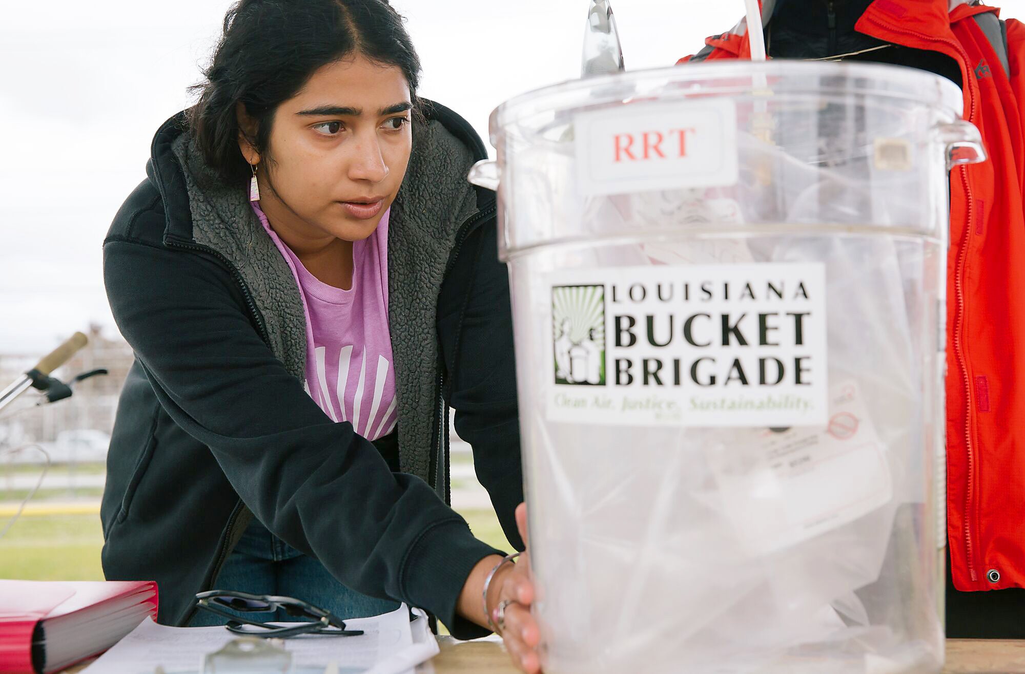 A woman examines a medium-sized clear bucket labeled "Louisiana Bucket Brigade"