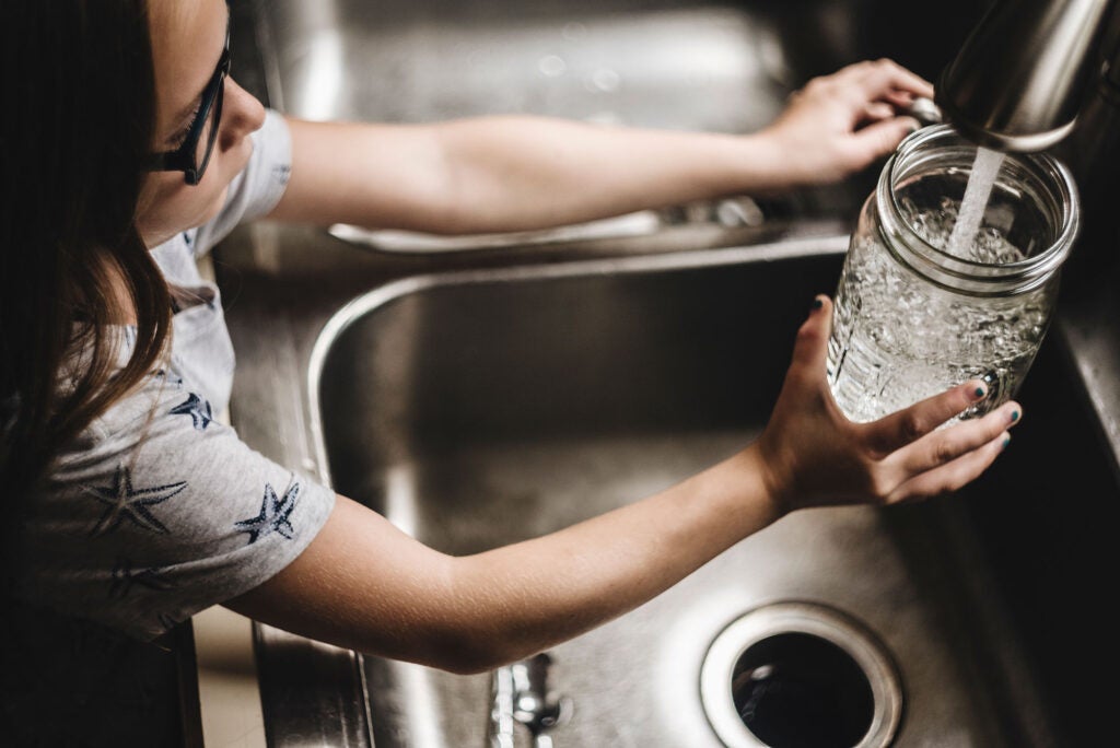 A child fills a drinking glass with water from the faucet. (Cavan Images)