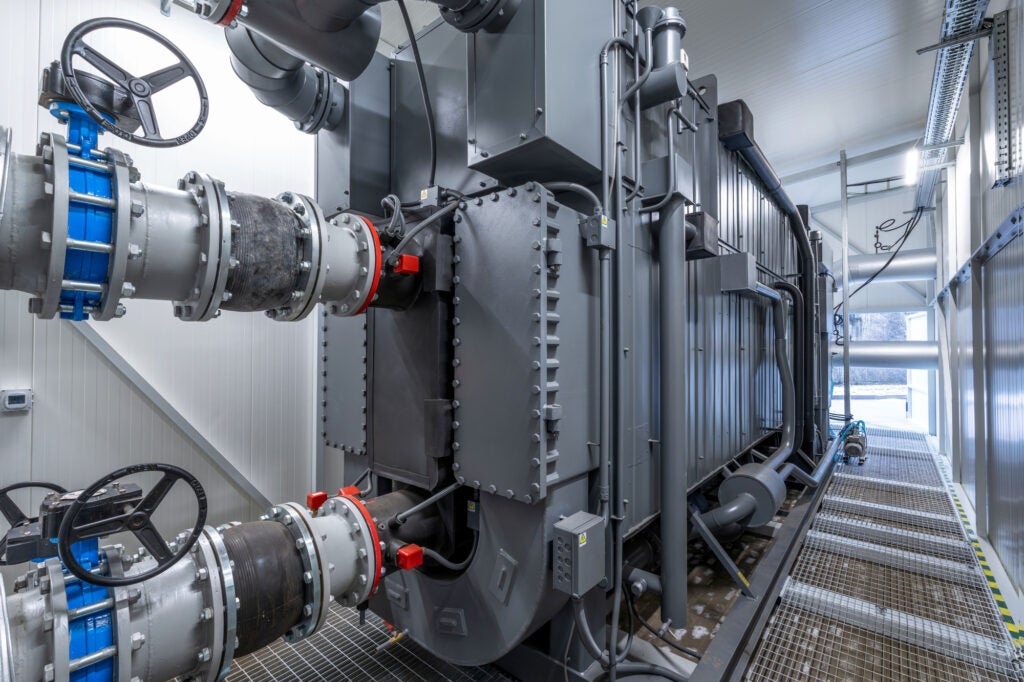 A large gray metal machine in a small room with several large pipes coming in and out of it.