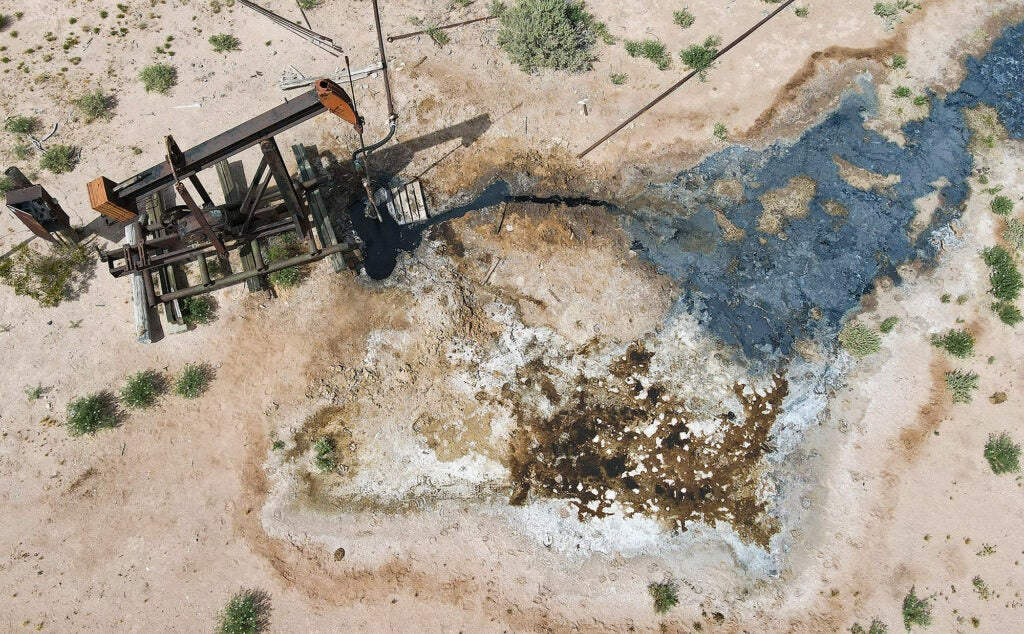 An aerial photo of a pump jack next to a pool of dark oil on the ground.