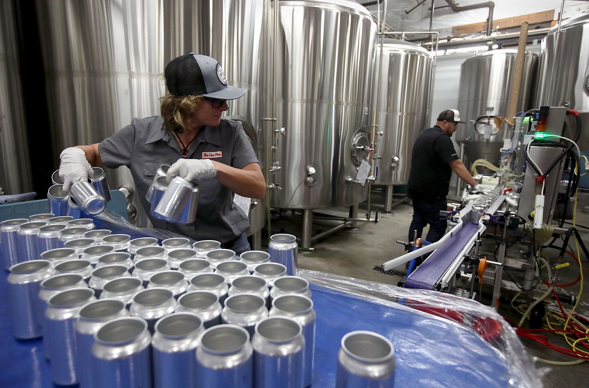 A person holds empty cans in a room full of large stainless steel tanks.